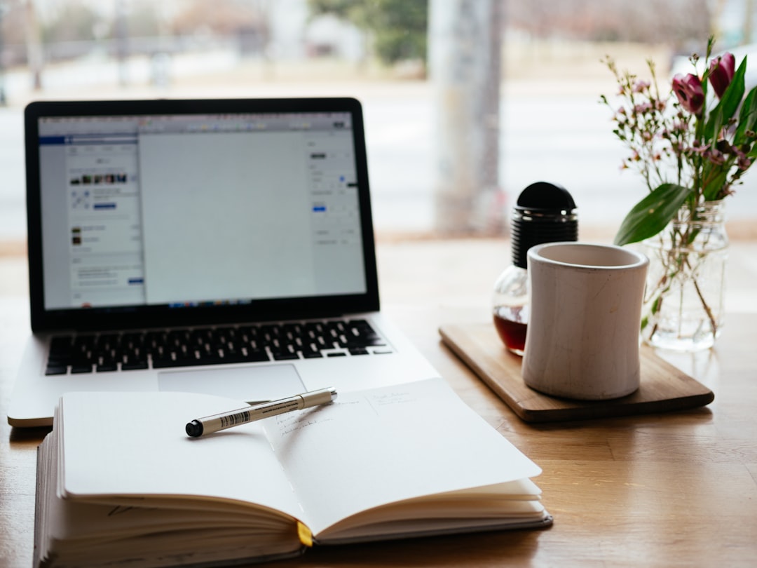 A person notes trading results in a physical journal next to the screen